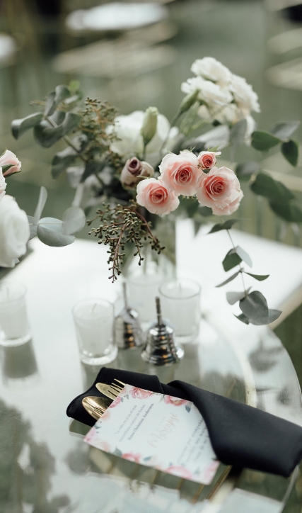 Decoración elegante de mesa con flores rosas, ramas de eucalipto, utensilios dorados y servilleta negra, ideal para eventos especiales.